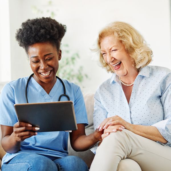 Nurse showing a tablet screen to senior woman and laughing at home