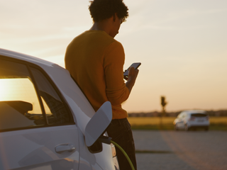 thumbnail black man using phone while charging his electric car