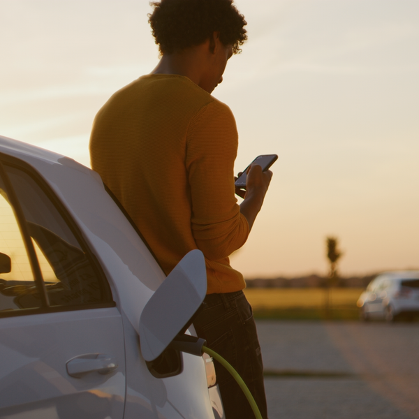 thumbnail black man using phone while charging his electric car