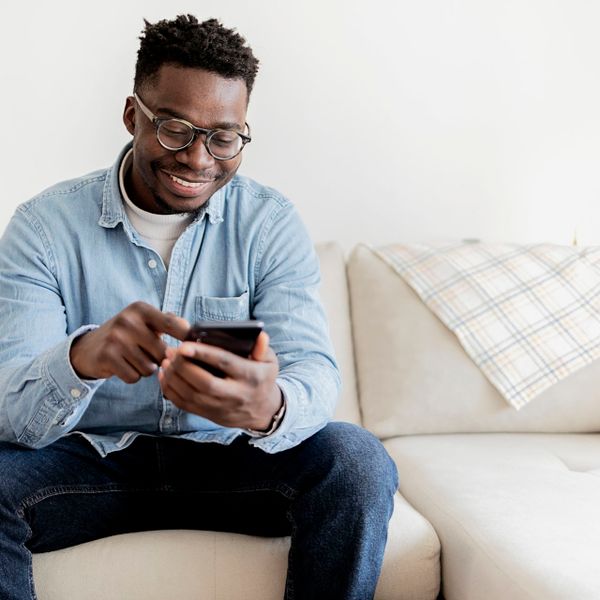 Black man at home texting on his smartphone while sitting on the sofa.