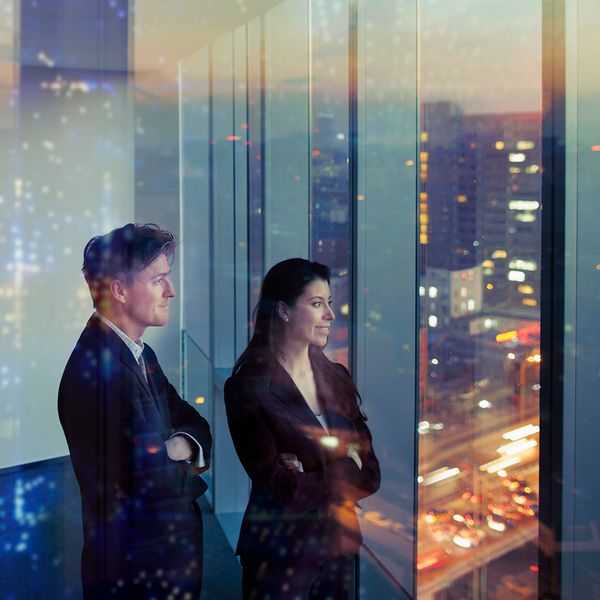 man and a women ceo stand looking further glass window.