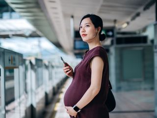 Foto de mulher oriental de cabelos presos, gr&aacute;vida segura o celular. 