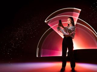 A woman stands and holds up her smartphone to take pictures, surrounded by light painting effects.
