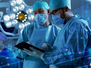 Doctors talking in an operating room, one of them holding a tablet