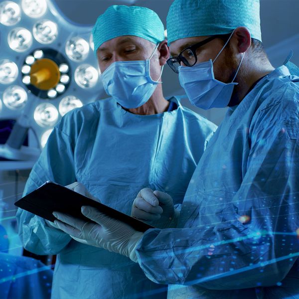Doctors talking in an operating room, one of them holding a tablet