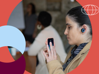 Empres&aacute;ria deficiente visual usando smartphone e fones de ouvido durante reuni&atilde;o de neg&oacute;cios