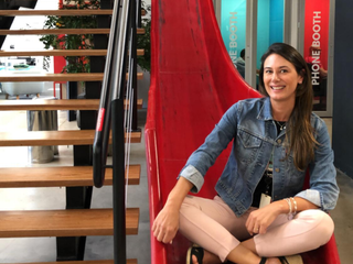 Fernanda Braga, mulher parda, de cabelo liso castanho e olhos pretos, sorrindo. Veste uma blusa preta e jaqueta azul.