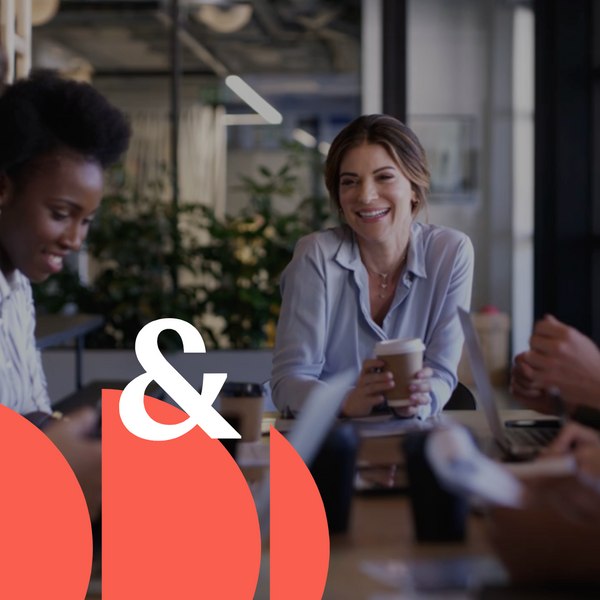 Equipe de pessoas sentados ao redor de uma mesa. Estão conversando e sorrindo um para os outros. 