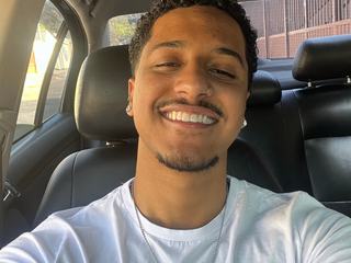 Maicon, homem pardo de cabelo preto cacheado, sorrindo.