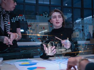 Two women looking at a computer with computer graphics in front of her