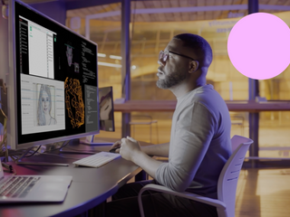 man working at night on a large computer screen showing AI avatars, chatbots & their production along with lines of computer code