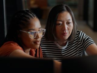 Two software engineers working together, analyzing code on computer screens in a bright, modern office environment
