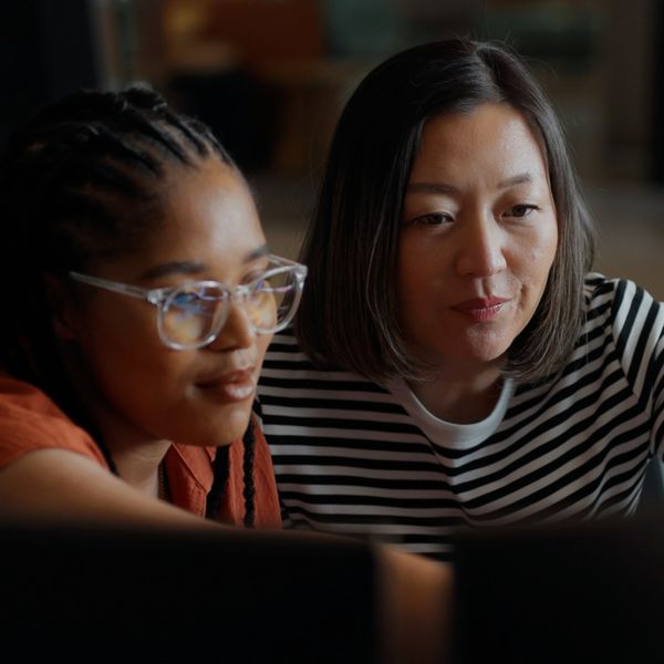 Two software engineers working together, analyzing code on computer screens in a bright, modern office environment