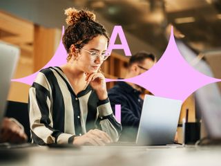 A woman wearing glasses and a striped shirt is working on a laptop in an office.