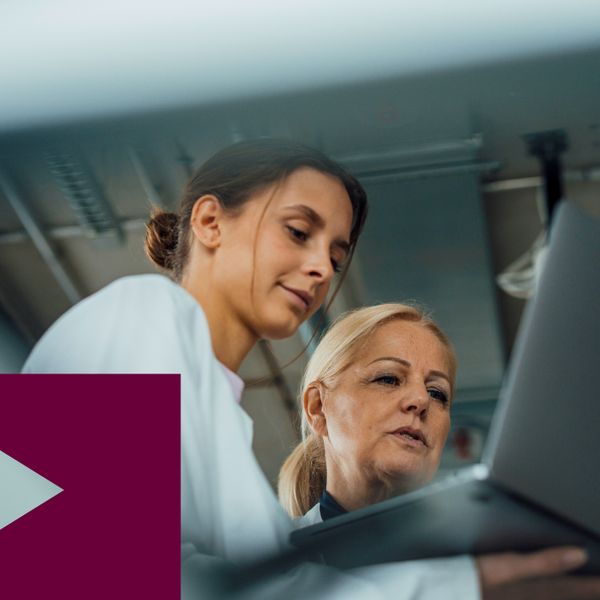 two women in lab coats reviewing information on a laptop in industrial setting