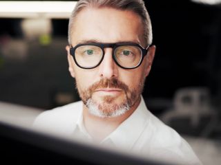 Man with glasses looking at a computer screen in an office environment.