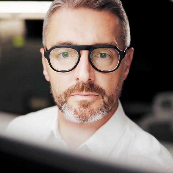 Man with glasses looking at a computer screen in an office environment.