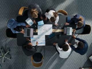 Overhead view of a diverse team in a meeting around a table with laptops and documents, focused on collaboration.