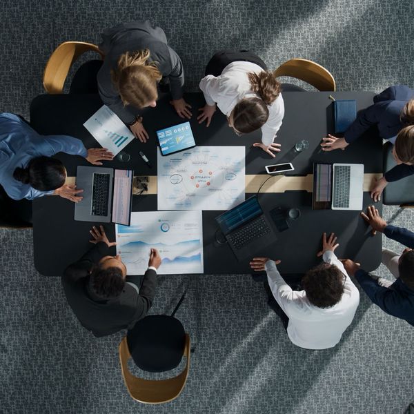 Overhead view of a diverse team in a meeting around a table with laptops and documents, focused on collaboration.