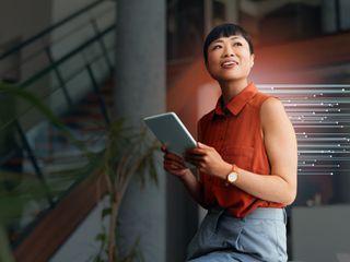  woman in a orange blouse holding a tablet and smiling in a contemporary office