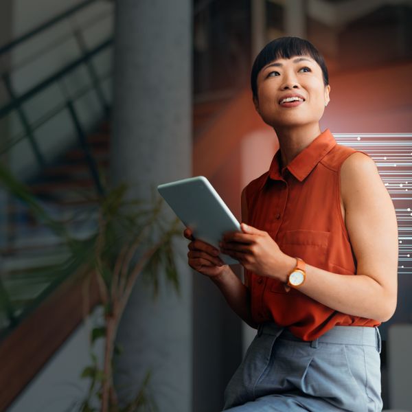  woman in a orange blouse holding a tablet and smiling in a contemporary office