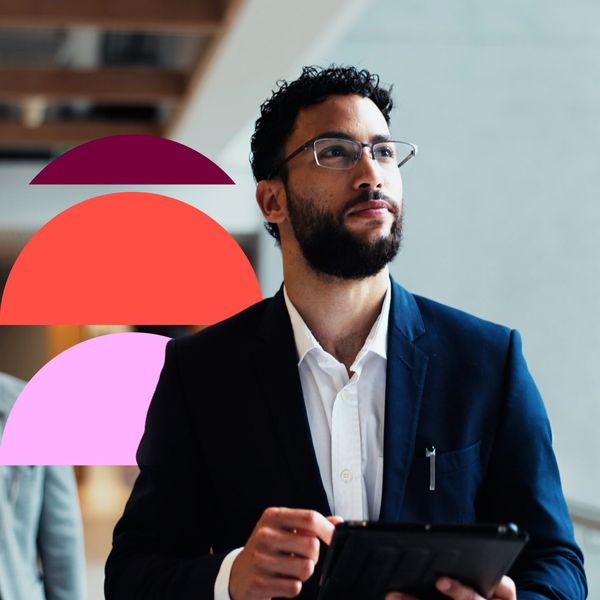 A forward-looking financial advisor in a suit walks through a modern office, using a tablet, with a colleague in the blurred background.