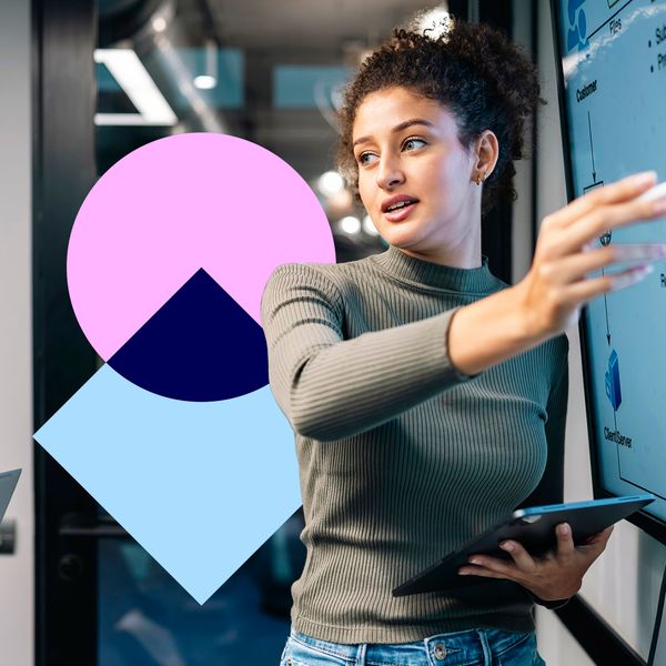 A professional woman pointing to a data flowchart on a large digital screen while holding a tablet in a modern office environment.