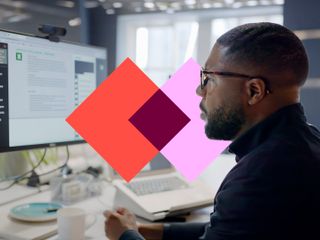 A man in glasses looks at a chatbot interface on a computer monitor, with a colorful geometric shape overlaid in the foreground.