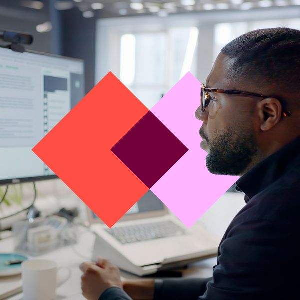 A man in glasses looks at a chatbot interface on a computer monitor, with a colorful geometric shape overlaid in the foreground.