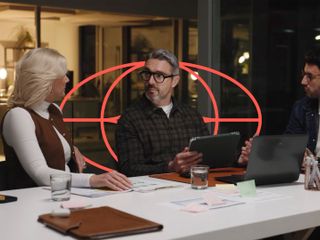 Three professionals engage in a focused meeting at a table with laptops and tablets in a modern office at night, featuring a red circular geometric overlay.