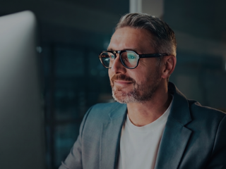 A man wearing glasses intently watching a computer screen.