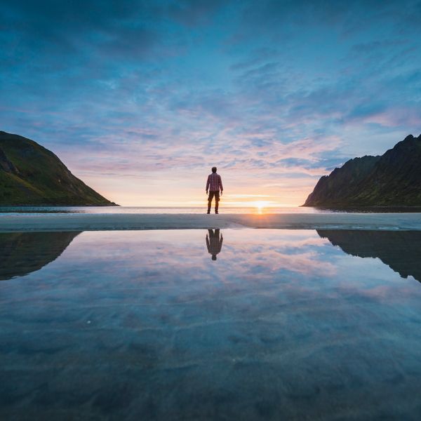 Person standing between mountains at sunset with reflections on the water