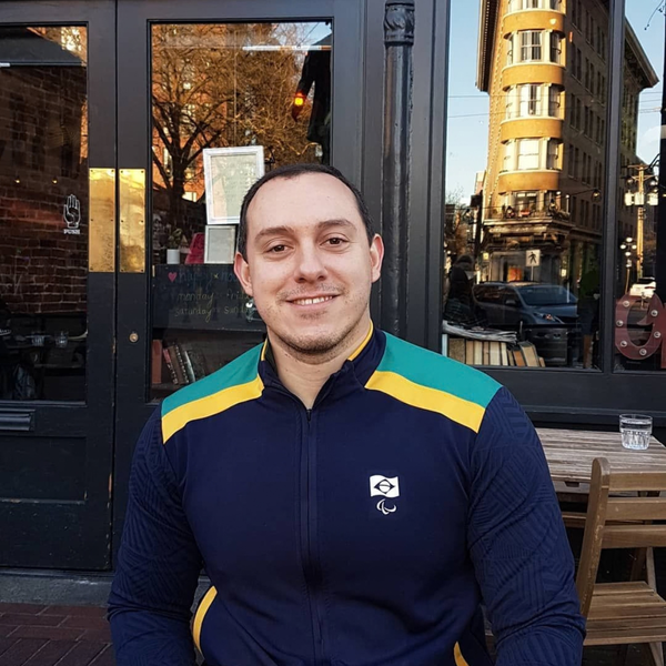 Daniel, homem branco de cabelo preto curto, sorrindo, veste um casaco azul marinho com a bandeira do Brasil e listras verde e amarelo.